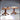 Digital render of two resin Games Table 01 scatter terrain pieces by Novaminis — pedestal tables with carved wood-grain bases and raised game board tops, one dressed with rows of rounded chess-style playing pieces and one showing a bare gridded board surface, shown side by side at an angle.