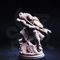 Unpainted grey resin miniature of Achtum of the Meadow, dwarven ranger, photographed from the front — showing crossbow, ornate round shield, layered armour including pauldrons and greaves, and a detailed textured base with foliage and rocky terrain