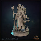 Agatha Saltwick miniature facing forward: hooded elderly woman gripping a staff in one hand and a merchant's balance scale in the other, with sacks and pots at her feet. Sculpt by Great Grimoire.
