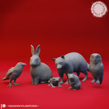 Digital render showing six of the woodland animal miniatures in closer detail — a raven, seated rabbit, foraging bear, frog, mouse, and barn owl — all unpainted grey sculpts against a red background by Yasashii Kyojin Studio
