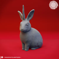 Close-up digital render of the jackalope miniature variant — a seated rabbit with small antler-like horns between its ears, unpainted grey sculpt, shown in detail against a red background by Yasashii Kyojin Studio