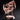 Front view of an unpainted salmon-pink resin miniature of a heavily armoured warrior construct mid-stride, wielding two large serrated scythe-axes swept wide, wearing ornate scale armour with a masked helm and a tattered cape, mounted on a sculpted cobblestone base with a display plinth