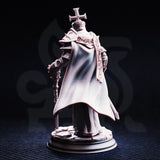 Rear-view photograph of the unpainted Arch Paladin Tyrius III miniature, showing the dramatic sweep of his full-length cloak, the back of his spiked pauldrons, and the detailed rubble base. The reliquary mace staff is visible at his side.
