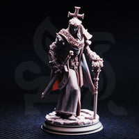 Front-view photograph of the unpainted Arch Paladin Tyrius III miniature against a dark background, showing the full detail of his chainmail robes, decorative stole, spiked pauldrons, cross headpiece, and ornate reliquary mace staff. The rubble base is clearly visible.