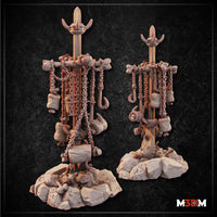 Two BBQ spit campfire terrain pieces by Mia Kay M3DM side by side — tall posts with crossbars hung with chains, hooks, sacks, and bones on rocky rubble bases. One base has sculpted flames.