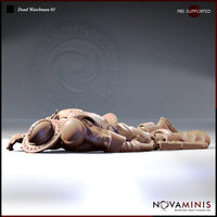 Digital render of Dead Watchman 01 miniature — an armoured city guard lying face-down on the ground, wearing studded leather armour, a nasal helm, and heavy boots, with a small round buckler beside him. Unpainted clay-toned resin render by Novaminis.