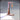 Digital render of Alarm Bell 01 scatter terrain by Novaminis — an L-shaped gallows-style wooden bell post with iron-banded joints, a hanging bell suspended by a chain with a clapper rope, mounted on a flat rectangular wooden base. Shown unpainted in warm pre-visualisation tones.