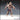Front-facing render of Gladiator 05 by Novaminis — an unpainted 32mm resin miniature of a muscular human male gladiator in a wide aggressive stance, wearing a spiked helmet, chain-wrapped torso, studded belt, and laced boots, wielding a spiked club in his left hand and a buckler punch-weapon in his right