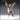 Front-facing digital render of Seated Arena Spectator 01 — a bald broad-shouldered man in a cross-stitched tunic and heavy boots, both arms thrown overhead in a cheering pose, mouth open wide, unpainted resin tan colouring