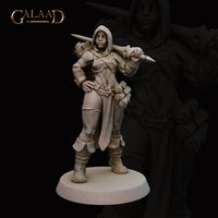 Front view of an unpainted grey resin miniature of a hooded female human battlemage, standing with one hand on her hip and a dagger levelled in her right hand, with a scroll or bolt quiver rising behind her shoulder and layered split coat with knee armour — 32mm scale by Galaad Miniatures