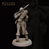 Rear three-quarter view of the same unpainted grey resin female battlemage miniature, showing a detailed scroll case strapped across her back, the hilt of a sword or dagger raised over her shoulder, layered armoured coat, and sturdy boots — 32mm scale by Galaad Miniatures