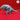 Grey resin Bulette miniature from Yasashii Kyojin Studio — front three-quarter view showing open jaws with curved fangs, layered armour plating across the back, four muscular clawed legs, and a shark-like tail fin, against a red background