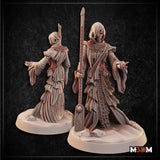 Hooded psychopomp figure in layered tattered robes gripping a tall rune-etched spear-staff, one hand outstretched with splayed fingers, scale-decorated mantle at the collar, standing on a rocky scatter base. Sculpt by Mia Kay M3DM.