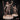 Bare-chested male figure holding a skull aloft in one raised hand and gripping a tall carved pole in the other, draped in flowing cloth, standing on a base scattered with bones and skulls. Sculpt by Mia Kay M3DM.
