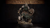 Armoured skeleton warrior striding forward over a base of skulls and cracked tombstones, clutching a lowered longsword and raising a battered round shield, wearing plate armour and a visored helmet with a tattered cloak. Sculpt by Atlanticus Arts.