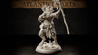Horned satyr miniature mid-stride, pan pipes raised to grinning lips and a gnarled staff lifted in his other hand, wearing tattered robes and rope belt with pouches, shaggy fur-covered legs ending in hooves, standing on a detailed forest floor base with mushrooms and a snail. Sculpt by Atlanticus Arts.