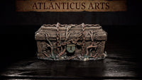 Weathered wooden chest covered in cracked wood grain texture, wrapped in heavy rusted chains and entwined with grasping roots and tendrils, with a verdigris-stained bronze lock plate at centre. Base of pebbles, moss, and roots. Sculpt by Atlanticus Arts.
