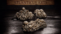 Three bone pile scatter terrain pieces by Atlanticus Arts: two mounded heaps of skulls and bones on rocky bases, one wide elongated piece with articulated skeletal remains including ribs and long bones.