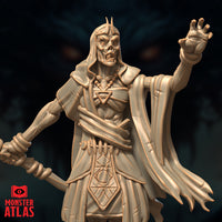 Close-up render of the Deathlock Mastermind miniature showing its skeletal face with horned crown, raised clawed hand, beaded amulet, and arcane-engraved tabard — unpainted gold-toned render by Monster Atlas