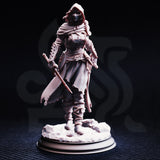 Front three-quarter view of the unpainted grey resin Delyna ro Unviel miniature on a round display base — showing her iron half-mask, deep hood, chainmail hauberk with crusader cross, serrated cleaver, off-hand dagger, and detailed rocky rubble base