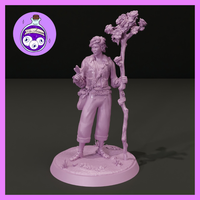 Digital render of an unpainted male Eladrin spring druid miniature at 32mm scale. He stands in a relaxed pose wearing loose travel clothes, sandals, and a vine braid across his torso. His right hand holds a butterfly and his left grips a tall wooden staff crowned with roses and wildflowers. The round base features scattered pebbles and small flowers.