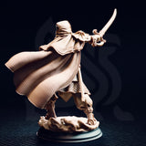 Elwahid Sword of the Sands miniature rear view — unpainted resin showing the finely textured woven fabric pattern on the back of the billowing cloak, scale armour on the lower legs, and the curved scimitar raised overhead.