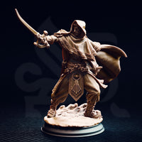 Elwahid Sword of the Sands miniature front view — unpainted resin desert elf in a deep hood, mid-lunge with curved blade extended, detailed carved tabard with sun emblem, on a round rocky base against a dark background.