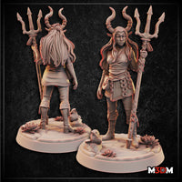 Female elf cleric standing upright, holding a tall staff topped with a three-pronged trident flanked by curved draconic horns. Long flowing hair, layered robes with rope belt and chain medallions, arcane markings on chest. Sculpt by Mia Kay M3DM — front and back views shown side by side on a rocky lotus-flower base.