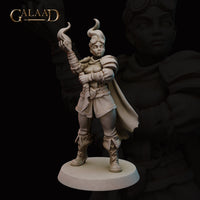 Unpainted grey resin miniature of a female human fire mage at 32mm scale, front view. She stands in a wide confident pose wearing layered armour with pauldrons, a long cape, and laced leather boots. One arm is raised with flame tendrils curling from her hand. Aviator goggles rest on her cap. Round base. Sculpted by Galaad Miniatures.