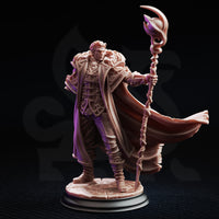 Frederik Vahlen Professor of Progress 32mm resin miniature by DM Stash — three-quarter front view showing unpainted grey resin sculpt with full detail of the layered coat, buckled chest harness, shin wrappings, the ornate twisted staff with glowing-orb finial, and the wide arc of the billowing cloak on a cracked stone integrated base