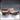Two rustic wooden double bed miniatures side by side — one with neatly laid sheets and two pillows, one with twisted rumpled sheets and a single displaced pillow. Wood-grain headboards with vertical striations. Novaminis.