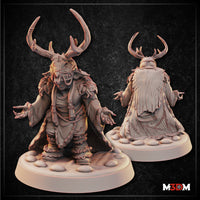 Goblin Shaman miniature by Mia Kay M3DM: hunched figure with both clawed hands raised, wearing antlered headdress, sinew face wrappings, layered fur and cloth robes bound with rope, on a cobblestone base. Front and rear views shown.