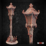 Digital render of the Gothic Garden Lamppost miniature showing the full piece from two angles — a tall rope-wound post topped with a latticed lantern head with swept pagoda-style roof, mounted on a cobblestone base overgrown with crystal formations and wild grass, shown in unpainted grey resin render