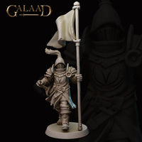Front view of an unpainted grey resin 32mm knight miniature from Galaad Miniatures — Queen's Guard 01 — showing full ornate plate armour with crested visor helm, floral pauldron detail, laminar leg armour, swept battle skirt, and a tall standard banner held in the right hand, striding forward on a round base