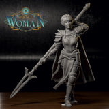 Photograph of a printed and unpainted grey resin Savine half-elf fighter miniature on a dark surface. The 32mm scale mini shows the same dynamic sword-raised pose with cape, layered armour, and braided hair. The level of detail in the chainmail, buckles, and sword grip is clearly visible in the physical print.