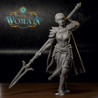 Photograph of a printed and unpainted grey resin Savine half-elf fighter miniature on a dark surface. The 32mm scale mini shows the same dynamic sword-raised pose with cape, layered armour, and braided hair. The level of detail in the chainmail, buckles, and sword grip is clearly visible in the physical print.