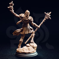 Studio photograph of the unpainted Hand of Seroca miniature from the rear, showing the back of her scaled hood and chainmail coif, layered back-plates, billowing skirt with woven texture detail, and the sun-star staff extending diagonally — the rocky terrain base clearly visible from this angle.