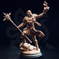 Studio photograph of the unpainted Hand of Seroca miniature in warm golden-beige resin, showing the full front view — masked elven face with pointed ears visible, detailed scale-textured chainmail, ornate plate armour, etched skirt panels, sun-burst staff totem, and open flame hand raised aloft, on a sculpted stone rubble base.