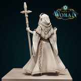 Rear of a hooded hexblood cleric miniature showing a sweeping cloak with full-length floral-scrollwork trim on the back panel and a star-burst sigil at the collar, gripping a tall staff aloft. Sculpt by DnD Is A Woman.
