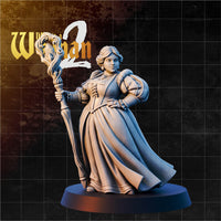 Full-length female wizard sculpt standing upright, holding a tall twisted staff in her right hand, left hand on hip. Long layered gown with laced corset bodice, puffed sleeves, and turban-style hair wrap. Sculpt by DnD is a Woman.