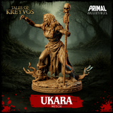 Ukara the swamp witch 32mm resin miniature — three-quarter view, standing tall with skeleton staff planted at her side and clawed hand raised, wild flowing hair, tattered robes with rope and bone detailing, skull-strewn base, unpainted tan resin, Tales of Kreyvos by Primal Collectibles