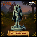 Sir Bedivere unpainted grey resin miniature, angled view from the front-left, standing with weight resting on a great sword planted in rocky debris, wearing layered plate and chainmail with a heavy draped cloak and helmet at his hip — Chronicles of Excalibur by Primal Collectibles