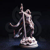Front view of unpainted grey resin Jeanne du Lac miniature on a dark background — showing her full plate armour detail, raised greatsword, long flowing hair, and scenic rocky base with debris.