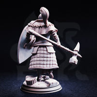 Rear view of the unpainted grey resin Jeremus of Jochenia miniature — showing the quilted scale-mail skirt, detailed back plate, feathered helm crest, and the engraved head of the war-hammer extended behind him, with the kite shield visible over his left shoulder