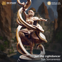 Juri the Lightdancer sun sorceress miniature by DM Stash — digital render showing the unpainted cream resin sculpt of a female elf mid-incantation, one arm raised with a spiralling ribbon of light magic curling above her, the other arm extended outward, wearing layered ornate robes with a wide sash, bracers, and jewellery, set on a decorative sunburst base, with canyon ruins in the background