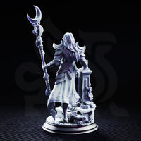 Kadna Glydrin by DM Stash — female elven warrior-mage standing on a vine-wrapped ruined stone base, holding a tall twisted staff topped with a crescent blade, wearing crescent pauldrons and filigree breastplate.