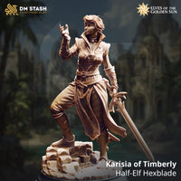 DM Stash product render of Karisia of Timberly, a half-elf Hexblade miniature — unpainted sculpt shown against a blurred jungle ruin background, one hand raised in an arcane gesture, the other holding an ornate longsword lowered at her side, wearing layered scale armour and a long split tabard over buckled boots, standing on a rubble stone base
