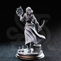Photograph of printed unpainted grey resin Kira Solseth miniature by DM Stash — rear three-quarter view showing billowing long coat, back detail of armour and belt straps, raised arcane orb, and curved blade at her side, with crate and potions on the scenic base