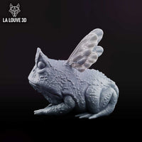 Cornuta Toad by La Louve 3D — squat warty toad viewed from the front, a single curved horn rising from its brow and a pair of veined insect wings spread behind its shoulders.