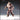Front-facing digital render of Creepy Assistant 01 by Novaminis — a large bald humanoid in stitched tunic and trousers with a rope belt, one hand fisted and one hand grasping, standing in a wide threatening stance with bare feet, unpainted grey resin render